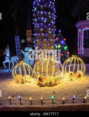 Beleuchtete Weihnachtsdekorationen im Freien mit Glühbirnen, großen Ornamenten, Weihnachtsbaum, Schneemann, Einhorn und beleuchteten Bäumen an einem Winterabend. Stockfoto