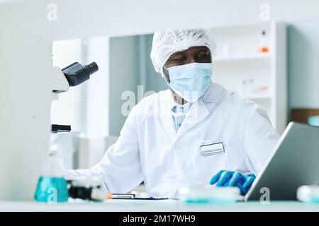 Portrait des schwarzen Mannes, der wissenschaftliche Forschung im Labor macht und Gesichtsmaske trägt Stockfoto