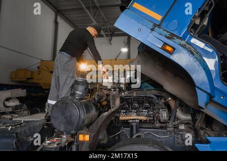 Automechaniker repariert großen Lkw oder Traktor in der Werkstatt. Professioneller Mechaniker repariert Lkw-Motor. Aufrichtiger Arbeiter. Stockfoto