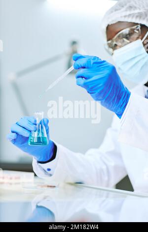 Vertikale Nahaufnahme eines afroamerikanischen Labortechnikers, der Flüssigkeitsproben mit einer Pipette nimmt Stockfoto