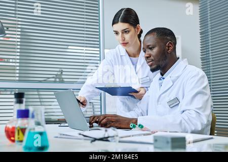 Porträt von zwei Wissenschaftlern, die Laptop benutzen, während sie Forschung im medizinischen Labor, Kopierraum Stockfoto