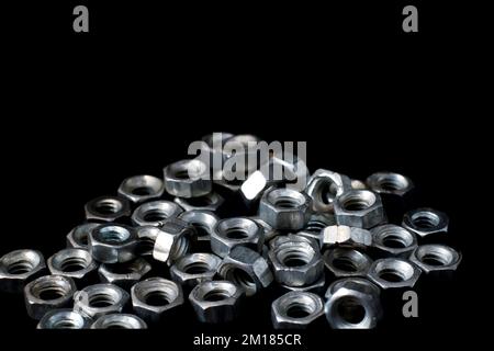 Glänzende Metallmuttern auf schwarzem Hintergrund, feuerverzinkte Metallmuttern, kurze Makromuttern und -Schrauben. Stockfoto