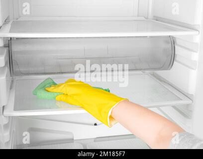 Kühlschrank mit Handreinigung. Person Waschen Kühlschrank mit Lappen. Die Zimmermädchen wischen die Regale mit dem sauberen Kühlschrank ab. Hand in gelbem Gummi-schutzfolie gl Stockfoto