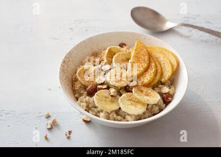 Köstliches, gesundes Frühstück. Haferflocken mit Banane, Apfel, Nüssen und Zimt auf hellgrauem Hintergrund Stockfoto
