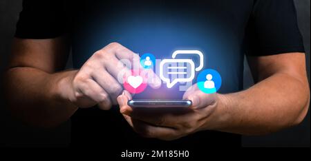 Ein Mann hält ein Smartphone mit virtuellem Social-Media-Symbol in der Hand. Männliche Hände und Handys mit Social Media und digitalem Online-Konzept. Nahaufnahme, dunkler Rücken Stockfoto