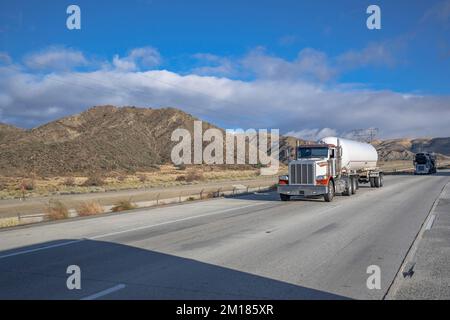 Klassischer brauner Sattelschlepper mit Chromzubehör transportiert entzündliche Chemikalien in einem sicheren Tank-Sattelanhänger, der auf der Geraden Autobahn fährt Stockfoto