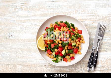 Gesunder veganer Salat mit Kichererbsen, Tomaten, Gurken, Paprika und Grünkohl auf hellem Holzhintergrund, flach liegend Stockfoto