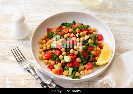 Gesunder veganer Salat mit Kichererbsen, Tomaten, Gurken, Paprika und Grünkohl auf hellem Holzhintergrund Stockfoto