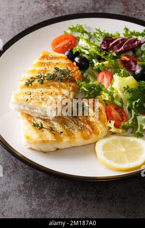 Gegrilltes Kabeljaufilet serviert mit frischem Gemüsesalat in Nahaufnahme auf einem Teller auf dem Tisch. Vertikal Stockfoto