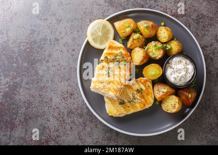 Gegrilltes Kabeljaufilet mit Thymian, serviert mit gebackenen Kartoffeln, Sahne-Sauce und Zitrone auf dem Tisch. Horizontale Draufsicht von oben Stockfoto