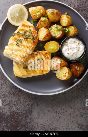 Gesundes Abendessen mit gegrilltem Weißfisch mit gebackenen Kartoffeln in Nahaufnahme auf einem Teller auf dem Tisch. Vertikale Draufsicht von oben Stockfoto