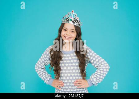 Heute will ich Prinzessin werden. Kleine Prinzessin lächelt blau hinterlegt. Prinzessin trägt Krone. Glückliche Prinzessin mit Schönheitsausdruck. Friseursalon. Mode Stockfoto