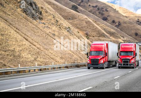 Team aus zwei professionellen, roten Sattelschleudern, die gewerbliche Fracht in Sattelanhängern transportieren, die zusammen auf der Multiline fahren Stockfoto