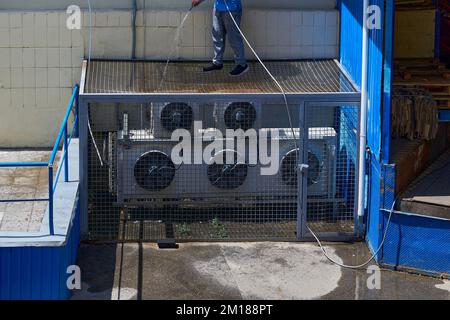 Ein Arbeiter wäscht die Klimaanlage im Garten einer Fabrik Stockfoto