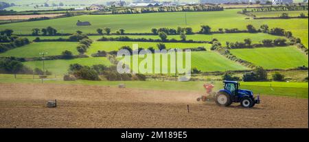 County Cork, Irland, 20. August 2022. Ein Traktor sät an einem Sommertag in Irland ein gepflügtes Feld. Landwirtschaftliche Arbeiten auf einem irischen Hof, landwirtschaftliche Flächen Stockfoto