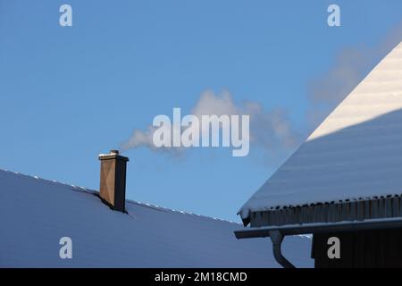 Ruderatshofen, Deutschland. 11.. Dezember 2022. Ein Rauchschornstein steht auf einem Dach, das mit frischem Schnee in der Sonne bedeckt ist. Kredit: Karl-Josef Hildenbrand/dpa/Alamy Live News Stockfoto