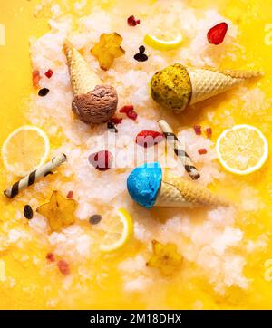 Bunte Eiskegel mit Früchten auf gelbem Hintergrund. Sommerliche Stimmung. Konzeptfotografie. Draufsicht. Für Hintergrundinformationen. Stockfoto