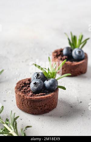 Zwei Schokoladen-Brownies mit Heidelbeeren und Rosmarin isoliert auf weißem strukturierten Hintergrund, Minimal Zusammensetzung dekoriert. Platz für Text. Vertikal oder Stockfoto