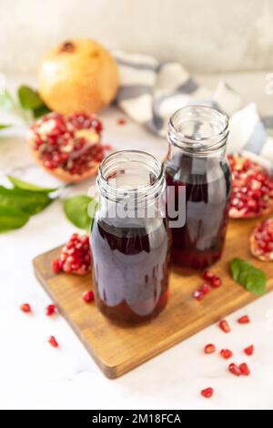 Gesunde Getränke Diät Immunität Vitamine oder vegetarisches Lebensmittelkonzept. Granatapfelsaft in Glasflaschen und frische Granatapfelfrüchte. Stockfoto