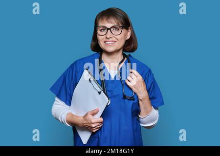 Porträt einer Ärztin mit Clipboard, die auf blauem Hintergrund auf die Kamera schaut Stockfoto