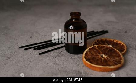 Zitrusreed-Diffusor auf dunklem Hintergrund. Für eine gemütliche Atmosphäre zu Hause. Flasche, Peitschen und trockene Orangen Stockfoto