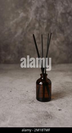 Aromatische Reed-Diffusorflasche mit schwarzen Stäben. Parfum für Zuhause. Trendkonzept. Vertikales Foto auf Marmorhintergrund Stockfoto