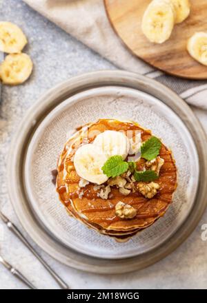 Zum Feiern des Pfannkuchen-Tages, amerikanisches hausgemachtes Frühstück. Glutenfreie Bananen-Pfannkuchen mit Nüssen und Karamell auf einer Tischplatte aus Stein. Blick von oben. Stockfoto