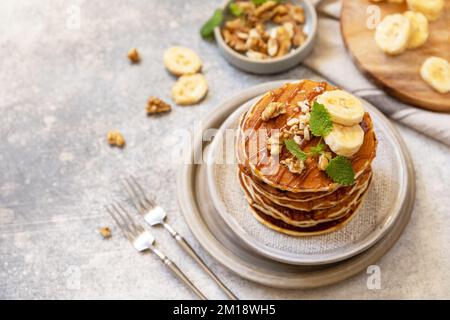 Zum Feiern des Pfannkuchen-Tages, amerikanisches hausgemachtes Frühstück. Glutenfreie Bananen-Pfannkuchen mit Nüssen und Karamell auf einer Tischplatte aus Stein. Stockfoto