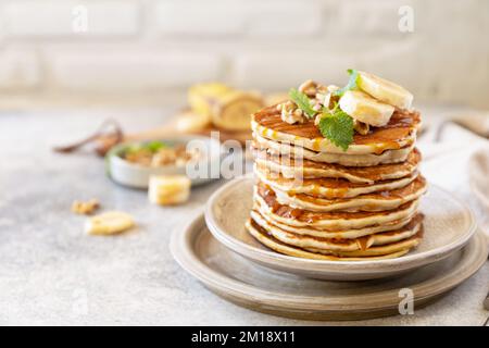 Zum Feiern des Pfannkuchen-Tages, amerikanisches hausgemachtes Frühstück. Glutenfreie Bananen-Pfannkuchen mit Nüssen und Karamell auf einer Tischplatte aus Stein. Stockfoto