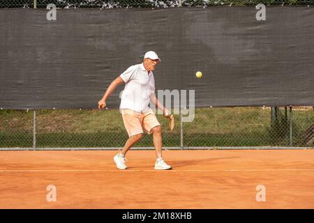 Senior-Tennisspieler in Sportbekleidung in Aktion auf einem Sandtennisplatz - Wellness-Konzept für Rentner Stockfoto