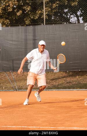 Senior-Tennisspieler in Sportbekleidung in Aktion auf einem Sandtennisplatz - Wellness-Konzept für Rentner Stockfoto