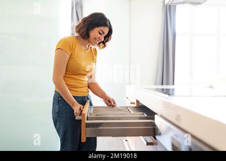 Junge araberin, die in der Schublade das Besteck aufräumt, während sie in der Küche putzt Stockfoto