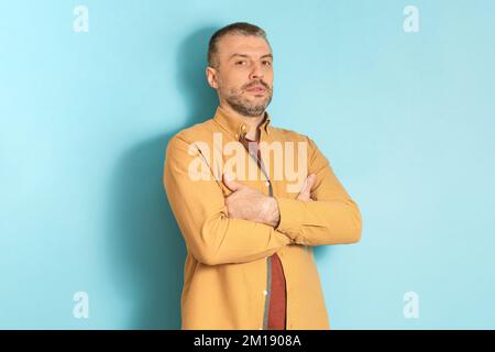 Das Konzept der menschlichen Emotionen. Porträt eines erwachsenen Mannes mit gefalteten Armen auf blauem Studiohintergrund Stockfoto