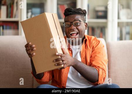 Aufgeregter fetter afrikanischer Kunde erhält gutes Paket, Heim-Innenraum Stockfoto