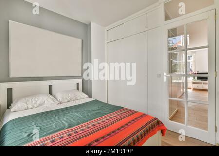 Ein Schlafzimmer mit einem Bett, Schränken und Glasschiebetüren, die zum Balkonbereich in einem Apartmentgebäude führen Stockfoto