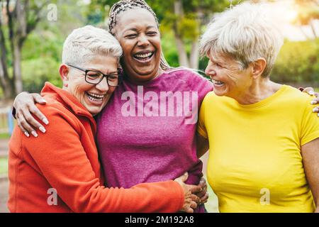 Multiethnische Seniorinnen, die nach dem Sport-Workout im Freien Spaß miteinander haben – Fokus auf linkes Frauengesicht Stockfoto
