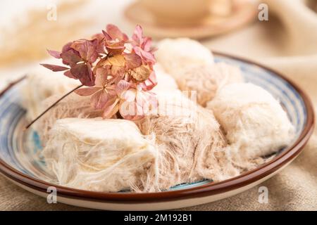 Traditionelle arabische Süßigkeiten Pishmanie und eine Tasse grüner Tee auf weißem Holzhintergrund und Leinentextilien. Seitenansicht, Nahaufnahme, selektiver Fokus. Stockfoto
