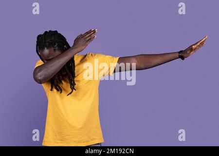 Ein cooler afrikanischer Mann in lässiger Optik, der Tanzbewegungen auf Lila zeigt Stockfoto