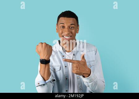 Glücklicher junger afroamerikanischer Mann, der mit dem Finger auf eine Smartwatch zeigt, mit leerem Bildschirm Stockfoto