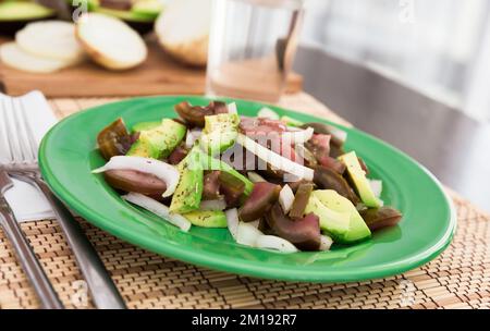 Salat aus schwarzen Tomaten, Avocado und Zwiebeln auf grünem Teller Stockfoto