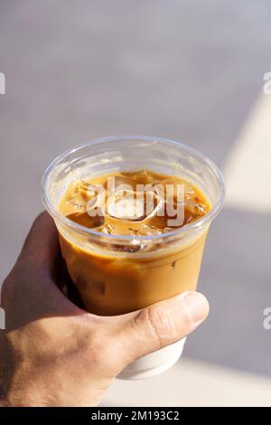 Eine Tasse Latte Cappuccino in der Hand auf der Straße der Stadt. Kaffeegetränk zum Mitnehmen. Hochwertiges Foto Stockfoto