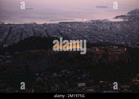 Ein Blick aus der Vogelperspektive auf die Akropolis auf einem Hügel, der in der Dämmerung in Athen, Griechenland, beleuchtet ist Stockfoto