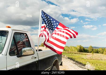 Die amerikanische Flagge, die im Sommer von einem guten alten Truck auf einer Landstraße fliegt Stockfoto