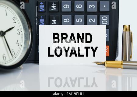 Geschäfts- und Finanzkonzept. Auf dem Tisch befinden sich eine Uhr, ein Stift, ein Taschenrechner und eine Visitenkarte, auf der der Text steht - MARKENTREUE Stockfoto