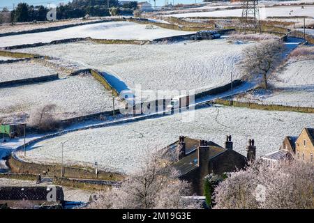 West Yorkshire, Großbritannien. 11.. Dezember 2022. Wetter in Großbritannien. Winterliche Szenen nach Schneefall über Nacht auf den Pennines in der Nähe von Queensbury, West Yorkshire, während Fahrer und Schafe den strahlend blauen Himmel und den wunderschönen Winterblick auf das Pennine Moor und die Landschaft genießen. Ein Lieferwagen der Sainsburys fährt auf einer engen, steilen Spur hinunter. Kredit: Windmill Images/Alamy Live News Stockfoto