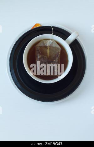 Kräutertee in einer weißen Tasse auf einer schwarzen Untertasse, abgebildet von oben. Stockfoto