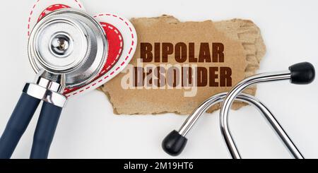 Medizin und Gesundheitskonzept. Auf einem weißen Tisch liegen ein Herz, ein Stethoskop und ein Karton mit der Inschrift - Bipolare Störung Stockfoto