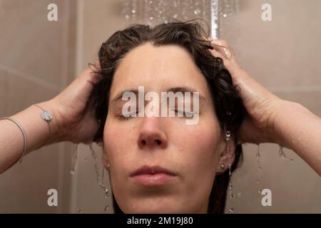 Eine Frau in ihren Dreißigern wäscht sich die Haare in der Dusche mit geschlossenen Augen. Konzept: An das Leben denken, entspannen Stockfoto