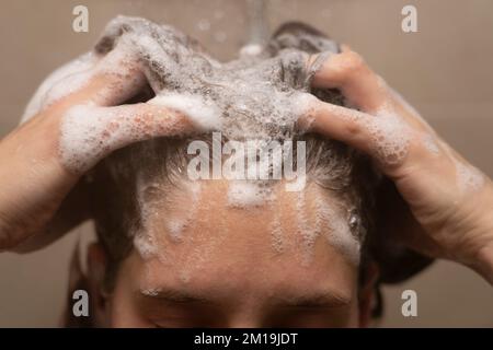 Nahaufnahme einer Frau in ihren Dreißigern, die ihr Haar unter der Dusche wäscht und sich Shampoo in die Haare reibt Stockfoto