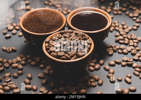 Frisch gemahlener und gebrühter schwarzer Kaffee auf schwarzem Hintergrund, drei Tassen mit gedämpftem Kaffee. Stockfoto